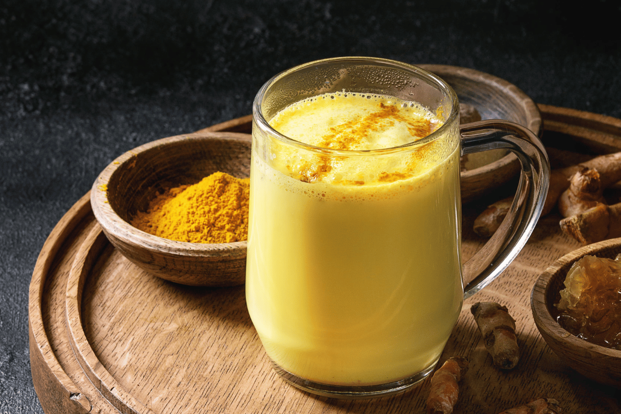 Ett träfat med ett ett glas golden milk och en träskål med gurkmejapulver